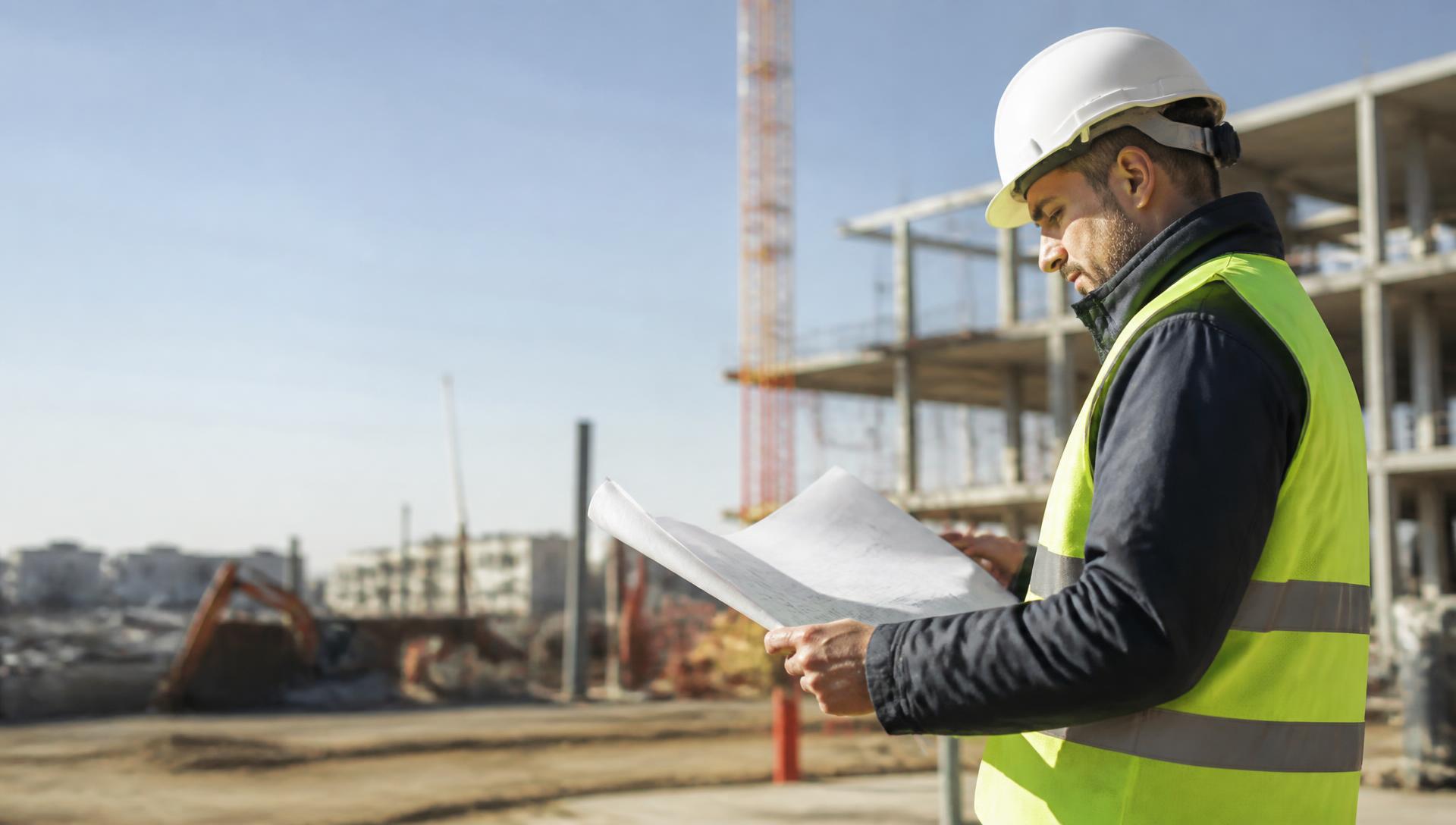 Engineer in hi-vis and hard hat reviewing technical drawings on site for an Engineers Australia assessment